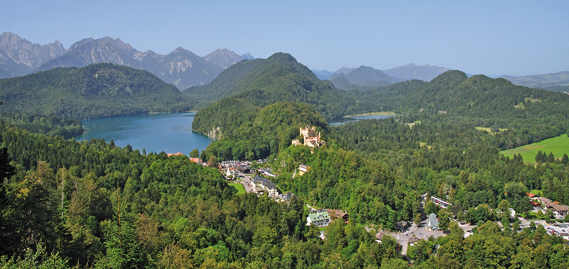 Landschaftsaufnahme von Hohenschwangau in Füssen, Allgäu, mit Schloss Hohenschwangau und umliegenden Wäldern und Bergen.