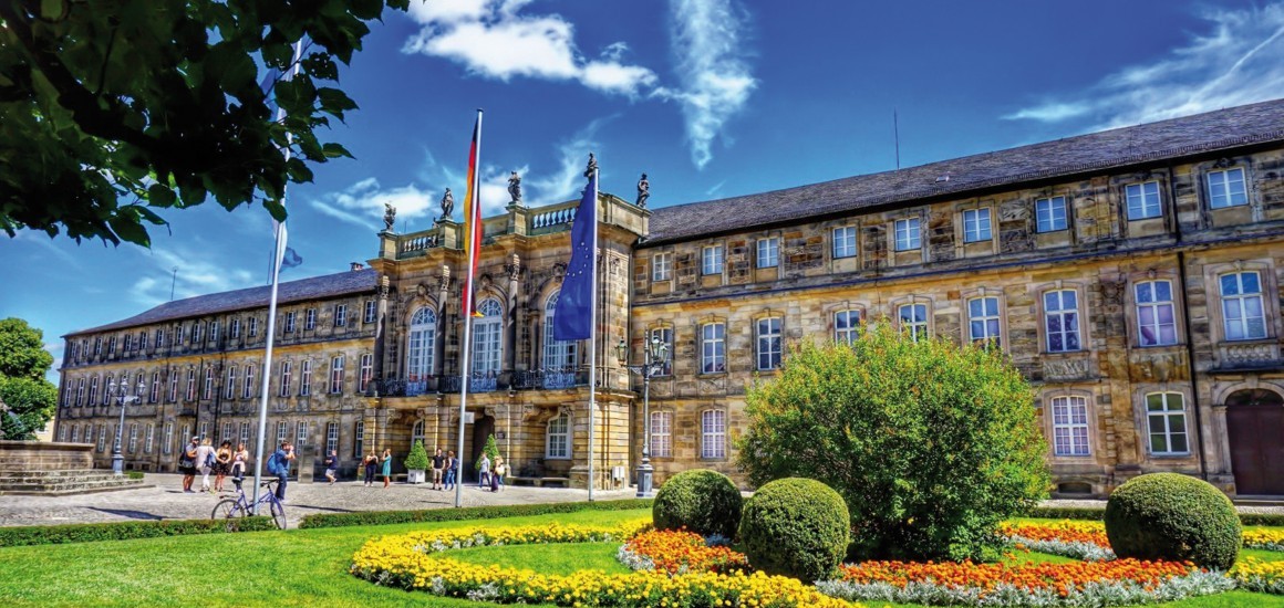 Neues Schloss mit gepflegtem Garten und Flaggen im Vordergrund