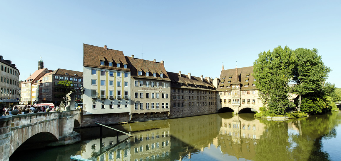 Panoramablick auf historische Gebäude entlang eines Flusses in Nürnberg, Bayern, mit einer Brücke im Vordergrund.