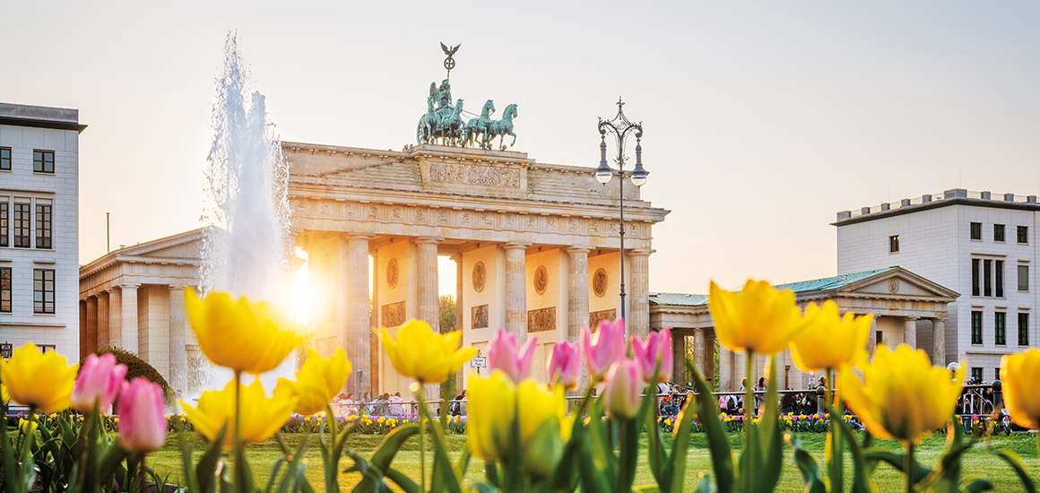 Brandenburger Tor in Berlin mit blühenden Tulpen im Vordergrund bei Sonnenuntergang.