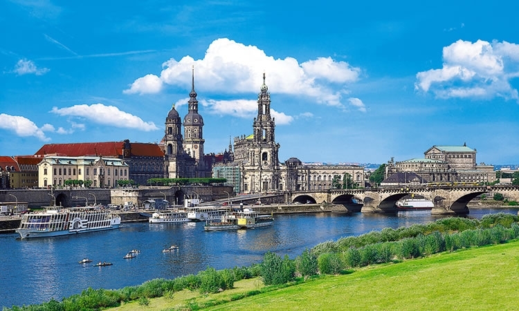 Stadtansicht von Dresden mit der Elbe im Vordergrund und historischen Gebäuden im Hintergrund, darunter die Frauenkirche und die Semperoper.