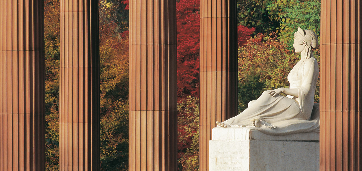 Statue vor Säulen in Bad Homburg, umgeben von herbstlichen Bäumen.