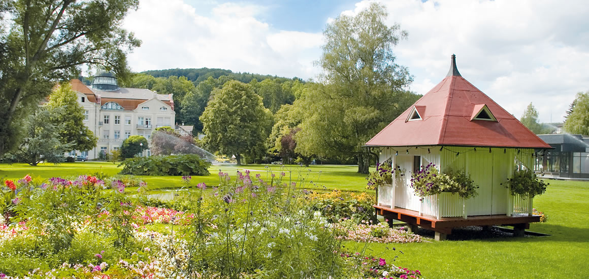 Ein gepflegter Park in Bad Salzschlirf mit einem kleinen Pavillon und einem großen Gebäude im Hintergrund.