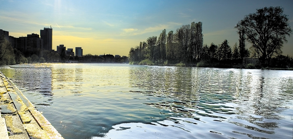 Flusslandschaft mit Bäumen und Gebäuden im Hintergrund, möglicherweise in Offenbach, Hessen.