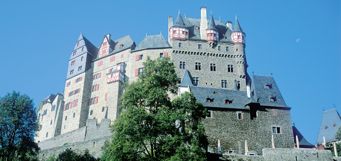 Burg Eltz vor blauem Himmel, umgeben von Bäumen