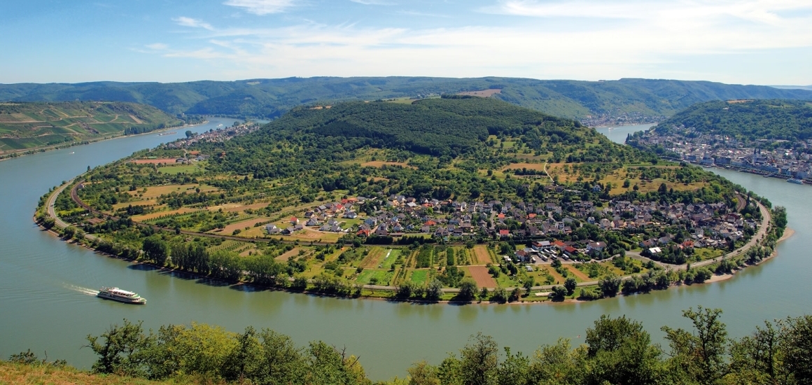 Panoramablick auf die Rheinschleife bei Boppard mit einem Fluss, der eine große Schleife bildet, umgeben von grünen Hügeln und einer Stadt am Ufer.