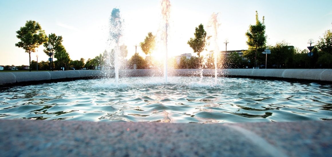 Springbrunnen im Kurpark von Bad Füssing bei Sonnenuntergang, umgeben von Bäumen.