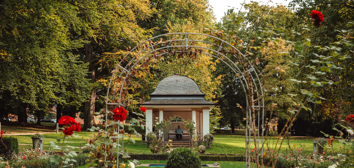 Ein Pavillon im Kurpark von Bad Nenndorf, umgeben von blühenden Rosen und Bäumen.