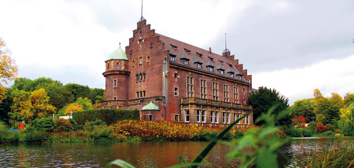 Wasserschloss Wittringen in Nordrhein-Westfalen, umgeben von Wasser und herbstlicher Vegetation.