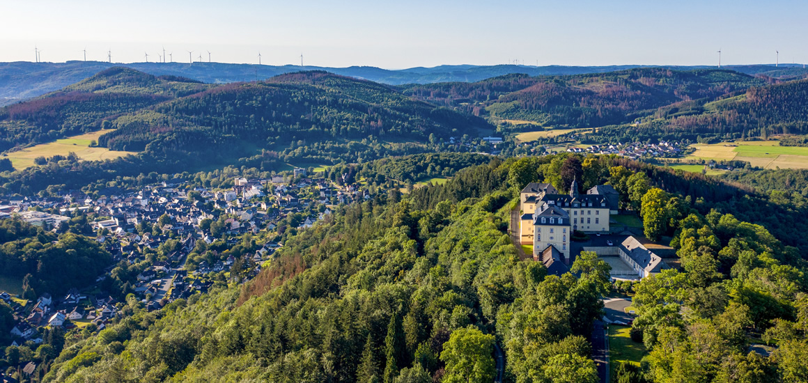 Luftaufnahme von Bad Laasphe in Nordrhein-Westfalen, umgeben von bewaldeten Hügeln und einem großen Gebäude auf einem Hügel.