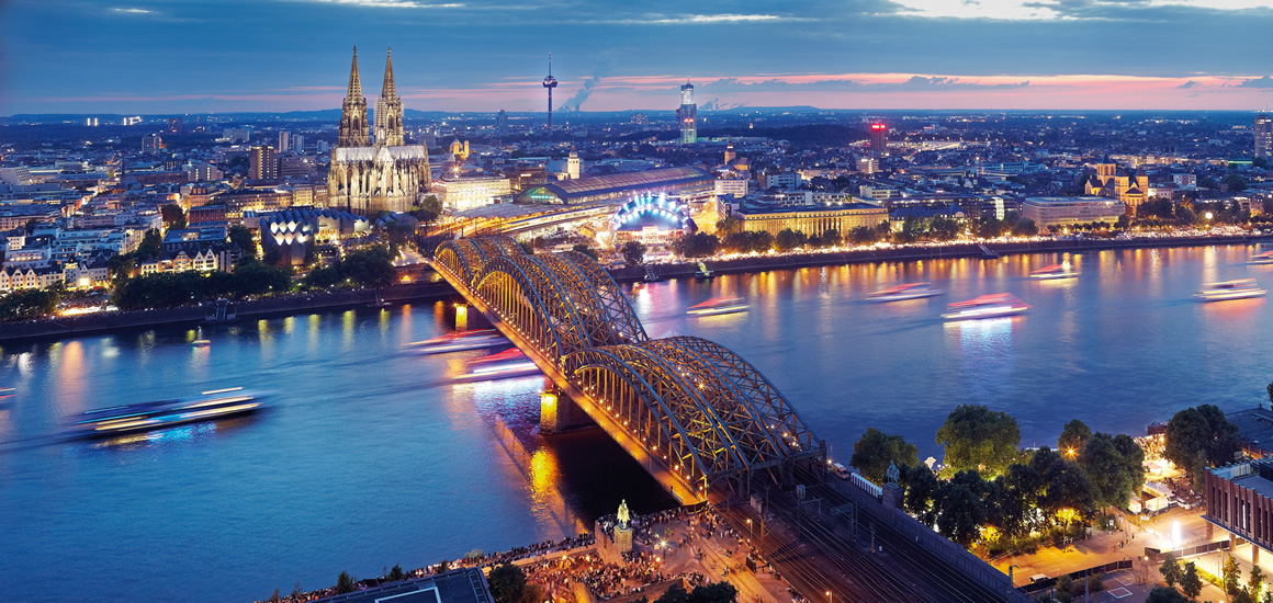 Panoramablick auf Köln mit dem Kölner Dom und der Hohenzollernbrücke bei Abenddämmerung.