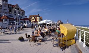 Strandpromenade mit Menschen, Tische, Strandkorb. 