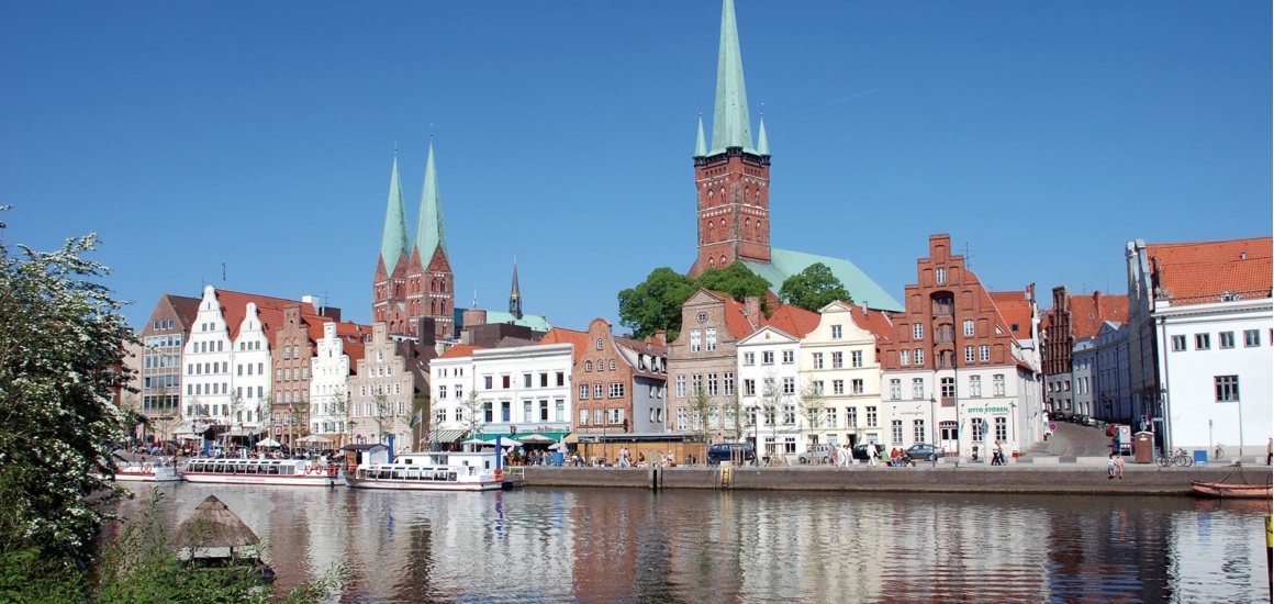 Blick auf die Altstadt von Lübeck mit der Trave im Vordergrund und den markanten Kirchtürmen im Hintergrund.
