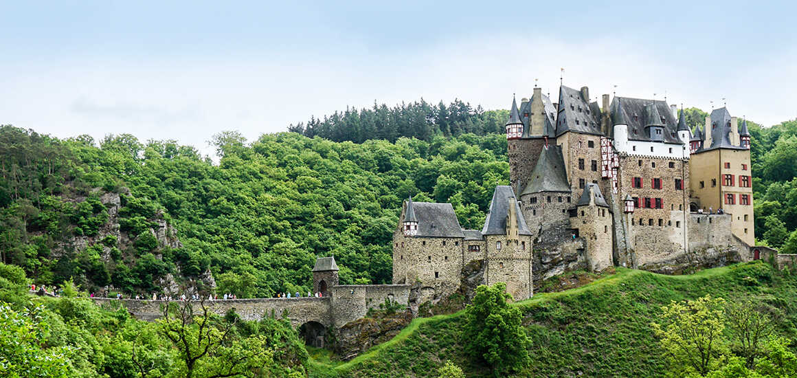 Burg Eltz vor blauem Himmel, umgeben von Bäumen