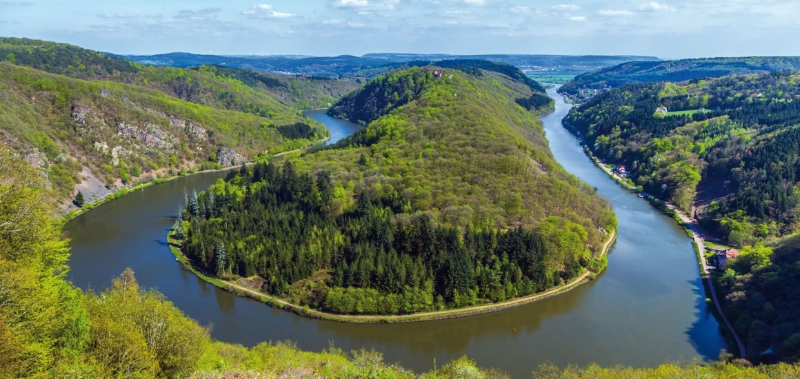 Luftaufnahme der Saarschleife, einer markanten Flussschleife der Saar, umgeben von bewaldeten Hügeln und grüner Landschaft.