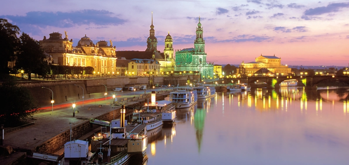 Nachtansicht von Dresden mit beleuchteten historischen Gebäuden und reflektierendem Wasser.