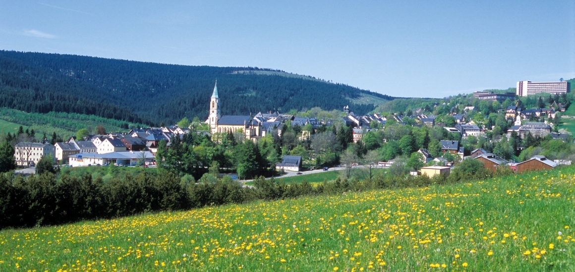 Panoramablick auf Oberwiesenthal mit Kirche und umliegenden Hügeln im Frühling.