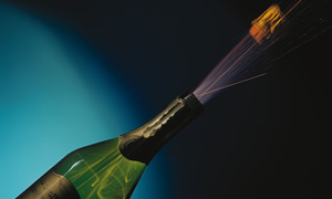 Eine Champagnerflasche, aus der ein Korken mit spritzendem Schaumverschluss fliegt.