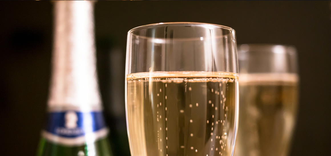 Zwei Gläser mit Sekt und eine Sektflasche im Hintergrund, typisch für Silvesterfeiern in Deutschland.