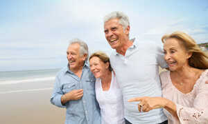 Strand mit Strandkörben und Menschen bei Sonnenuntergang, Wellen treffen auf den Sand.