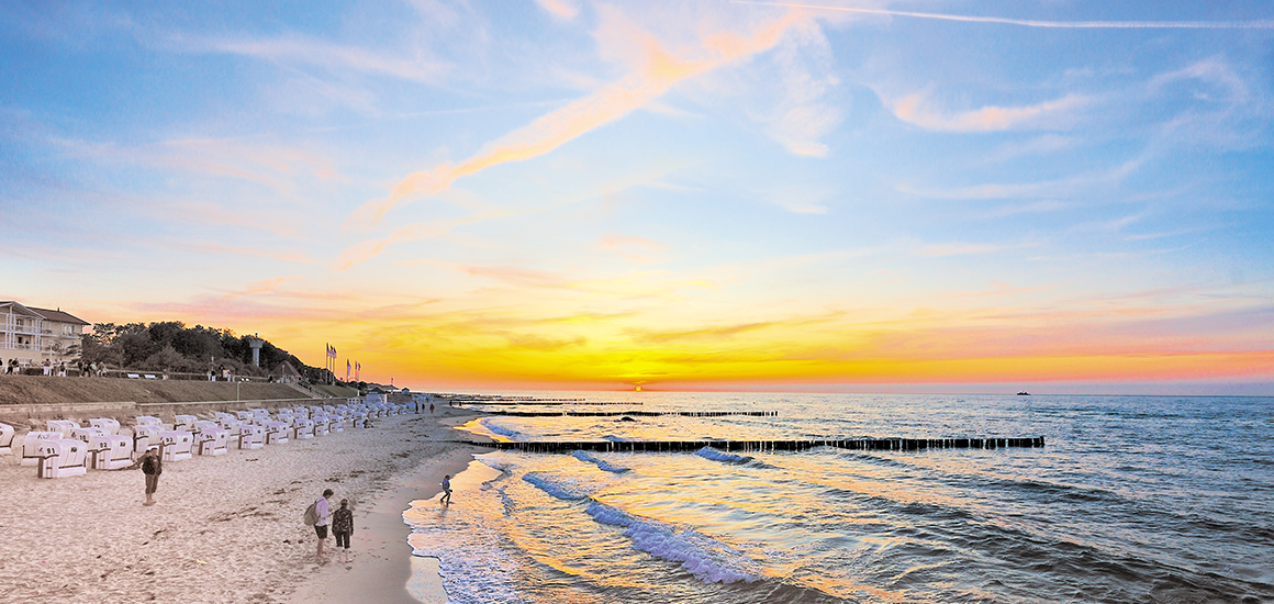 Strandansicht an der Ostsee bei Sonnenuntergang mit Strandkörben und Wellen am Ufer.