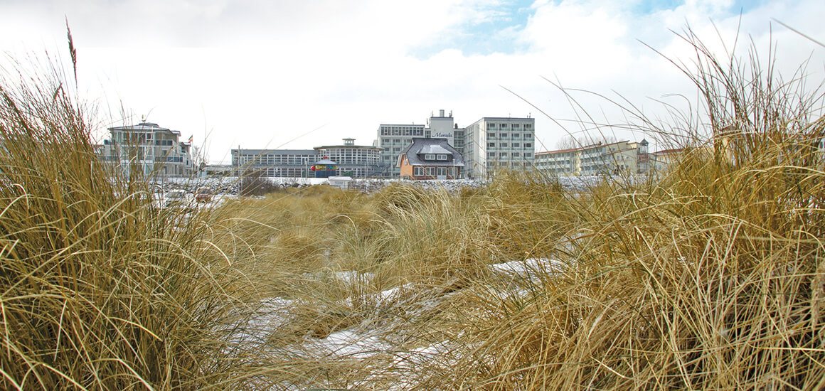 Winterlandschaft mit schneebedeckten Dünen und Gebäuden im Hintergrund