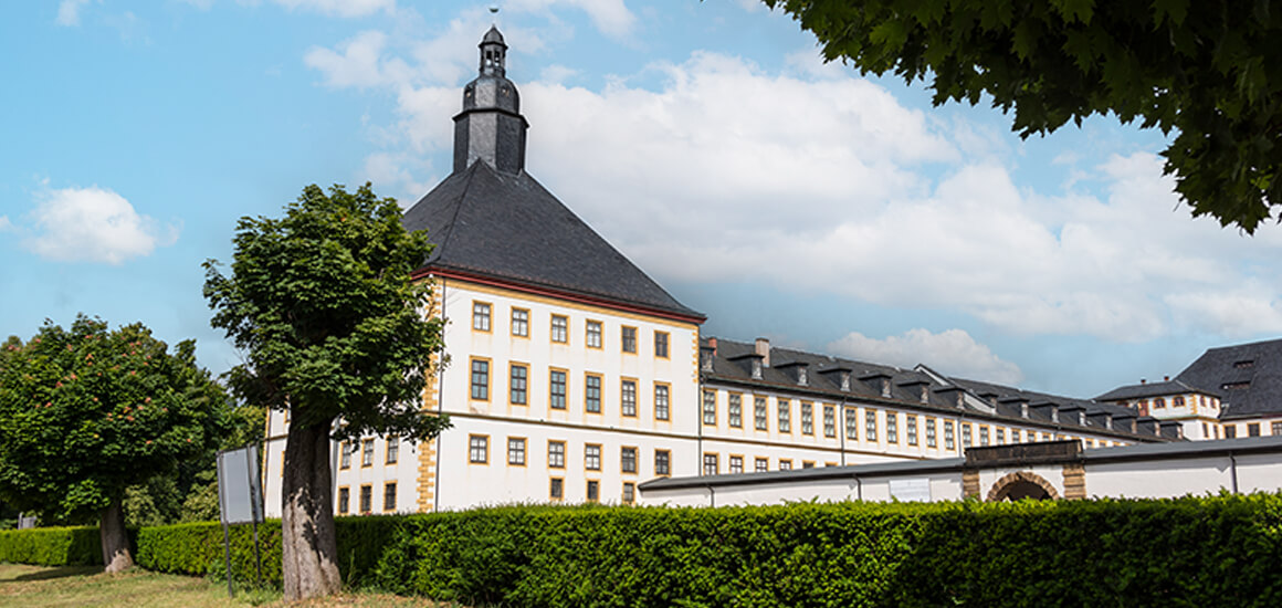 Schloss Friedenstein in Thüringen, Deutschland, mit einem großen Gebäude im Barockstil, umgeben von Bäumen und Hecken.