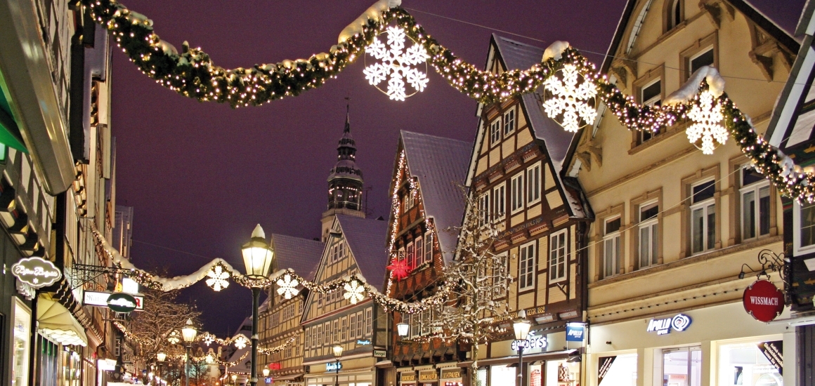 Eine verschneite Altstadtstraße in Celle, Deutschland, geschmückt mit Weihnachtsbeleuchtung. Fachwerkhäuser säumen die Straße, und Lichterketten mit Schneeflockenmotiven hängen über der Straße.
