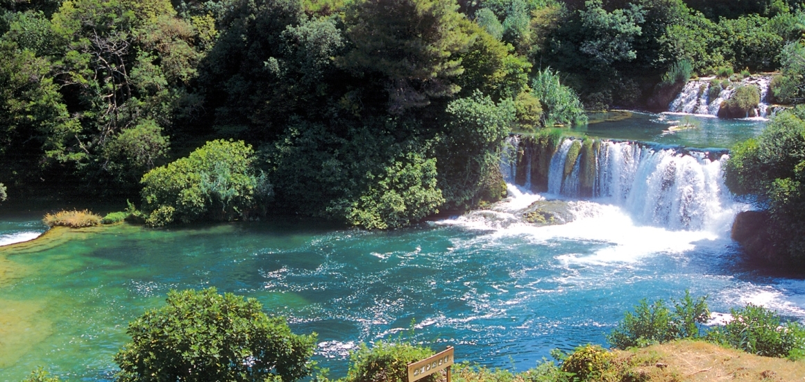 Ein Wasserfall in einer grünen, bewaldeten Umgebung mit klarem, türkisfarbenem Wasser, vermutlich in Kroatien.