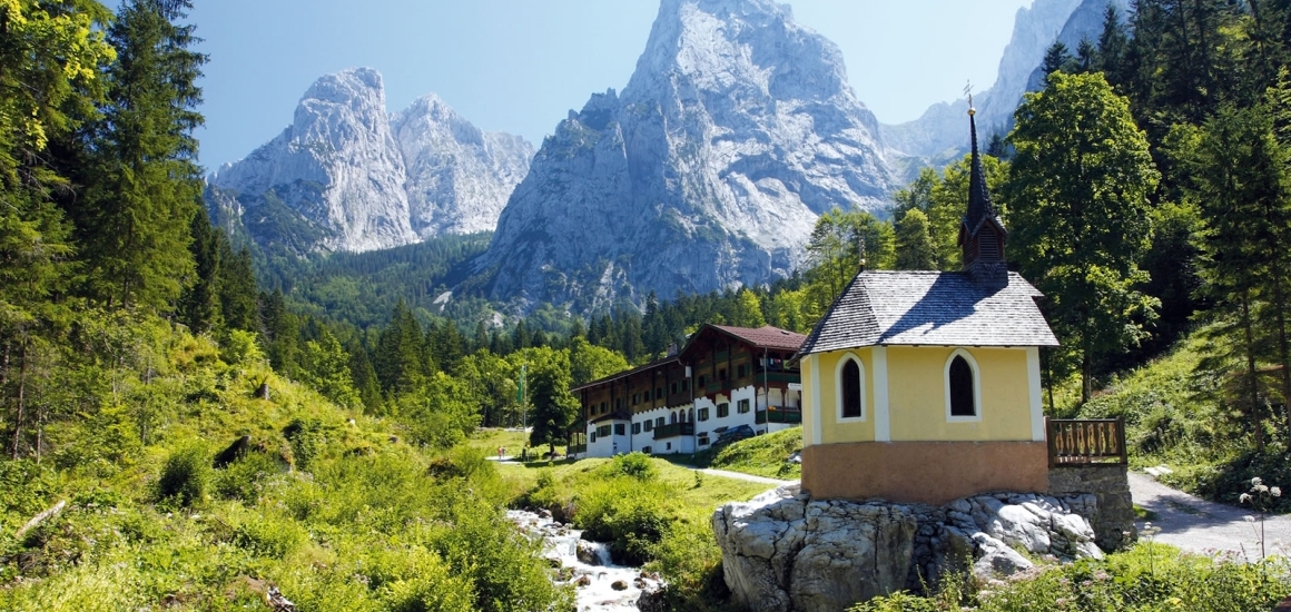 Eine malerische Landschaft im Kaisergebirge, Tirol, mit einer kleinen Kapelle im Vordergrund und beeindruckenden Berggipfeln im Hintergrund.