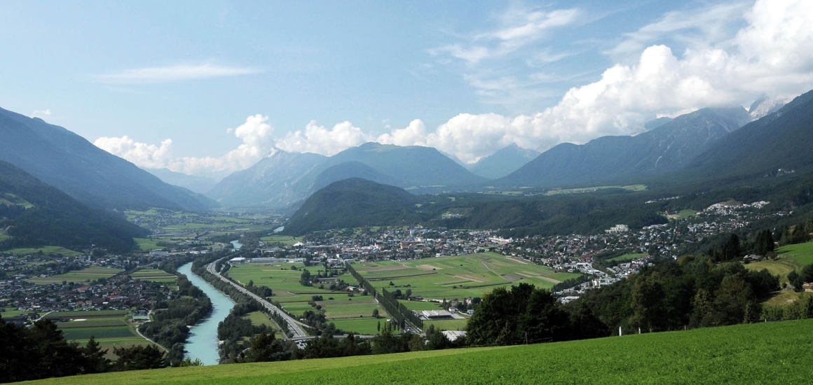 Panoramablick auf Telfs in Österreich, umgeben von beeindruckenden Alpenbergen unter einem klaren blauen Himmel.