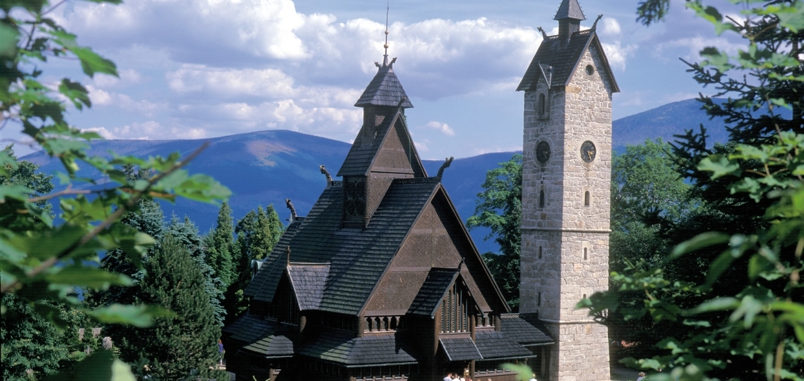 Holzkirche Wang in Karpacz, umgeben von Bäumen und Bergen im Hintergrund.
