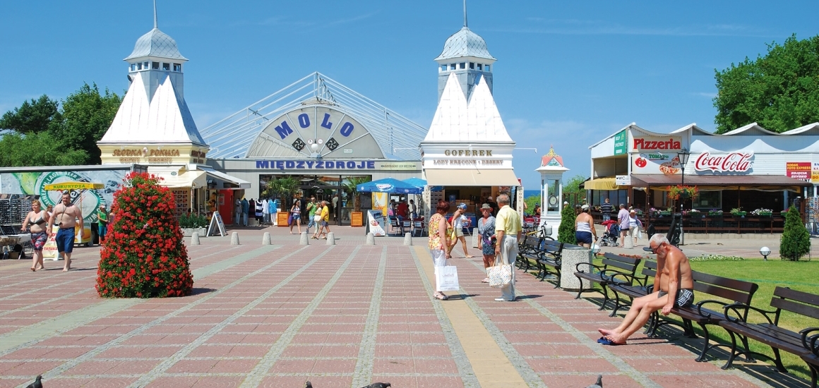 Eingangsbereich der Mole in Misdroy mit Menschen, die spazieren gehen und Geschäften im Hintergrund.