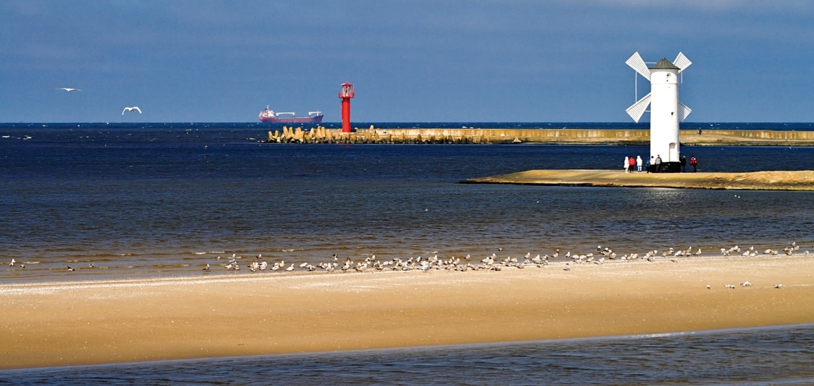 Strand mit Leuchtturm in Swinemünde, Polen, im Hintergrund ein roter Leuchtturm und das Meer.