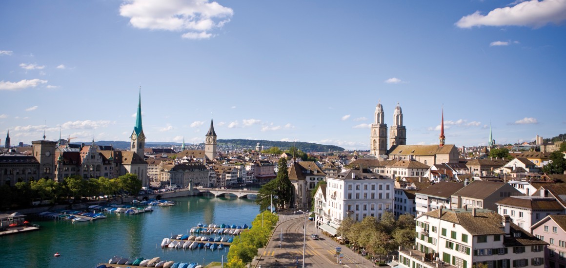 Panoramablick auf Zürich mit der Limmat, Kirchen und historischen Gebäuden unter einem blauen Himmel mit einigen Wolken.