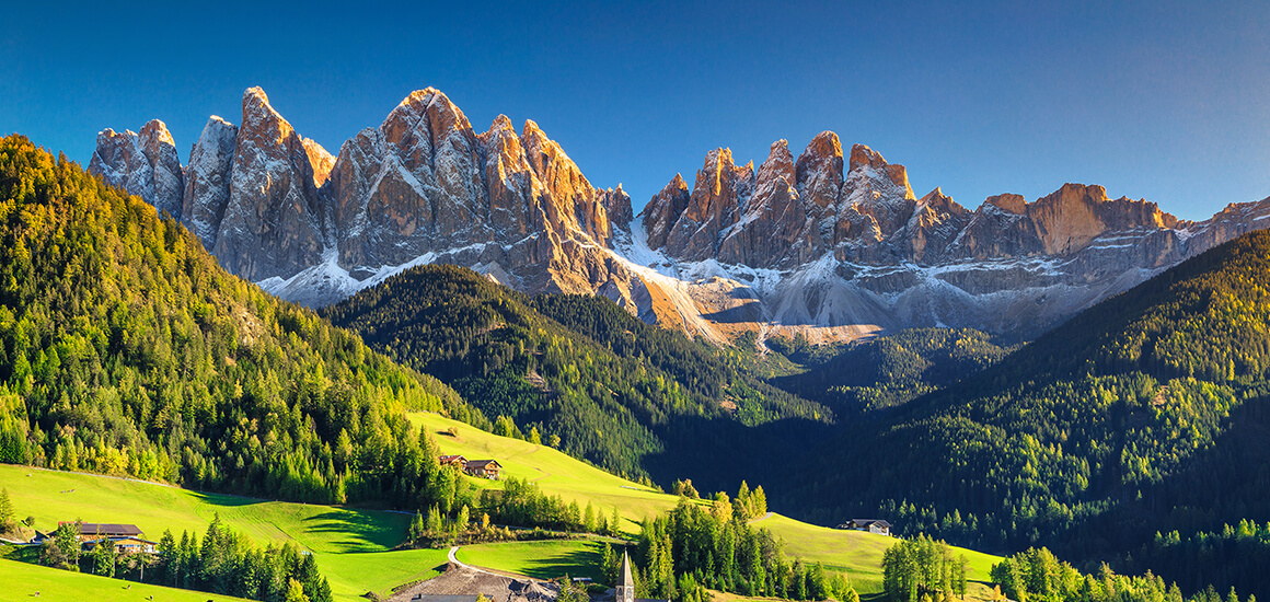 Panoramablick auf die Dolomiten in Südtirol mit grünen Tälern und bewaldeten Hügeln im Vordergrund.